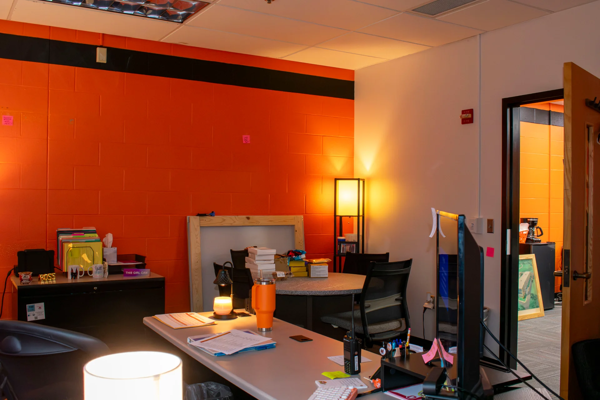 Warm lamp light on new orange-painted block walls in a Beavercreek school office as furnishings are moved back in