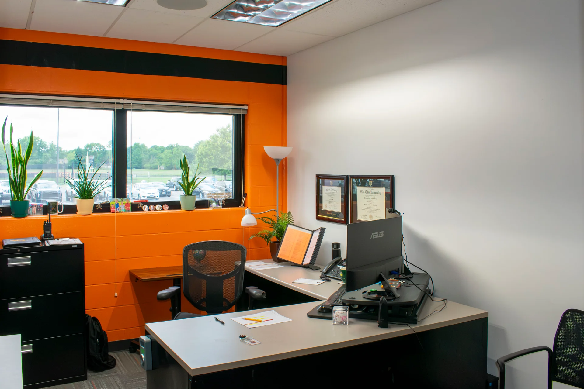 Administrator's desk beside a window in a repainted office at Beavercreek High School, with plants and framed diplomas back in place