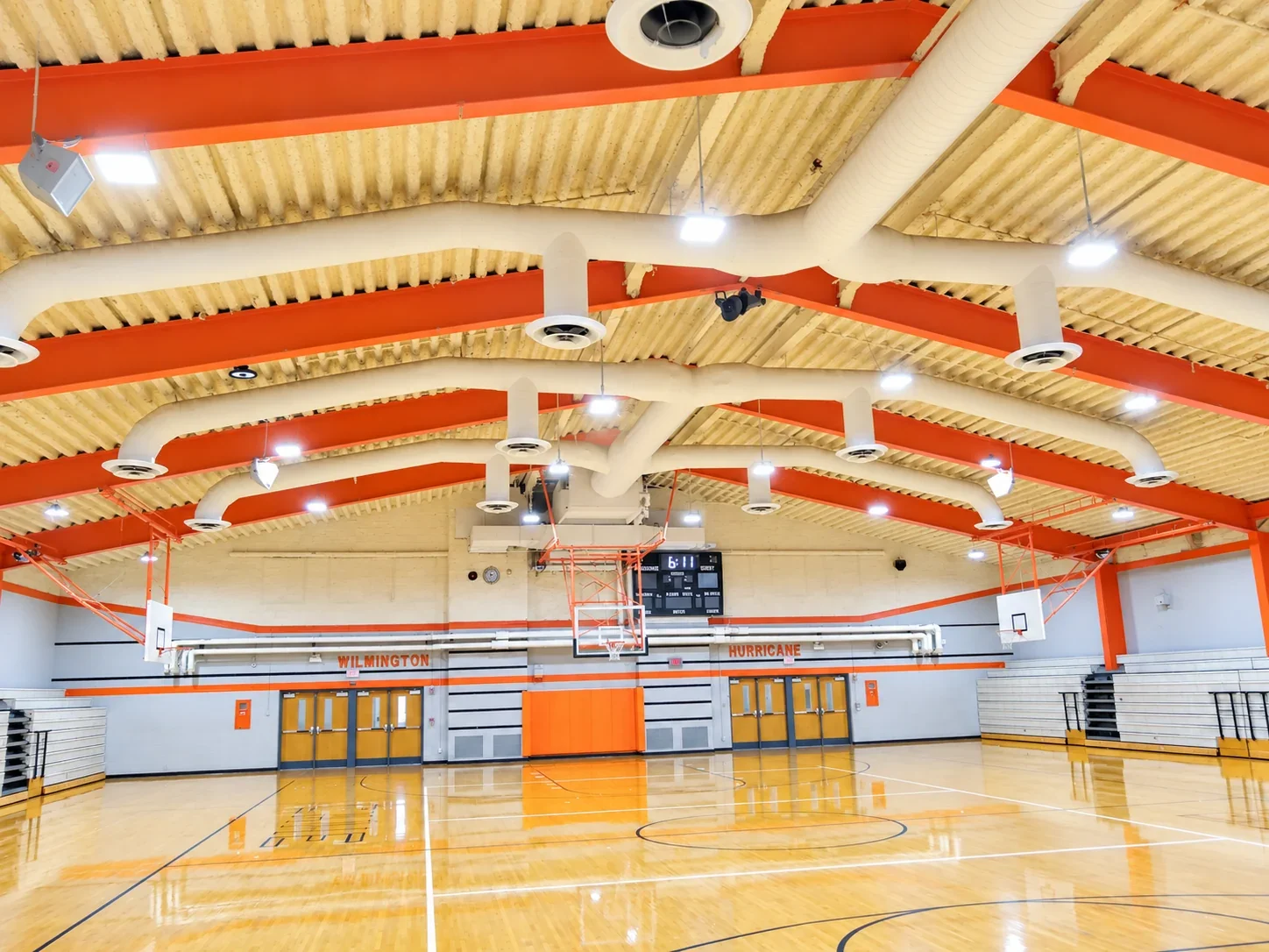Auxiliary gym on the Wilmington high school and middle school campus lit by new LED high bays between orange roof beams, with Wilmington Hurricane lettering on the far wall