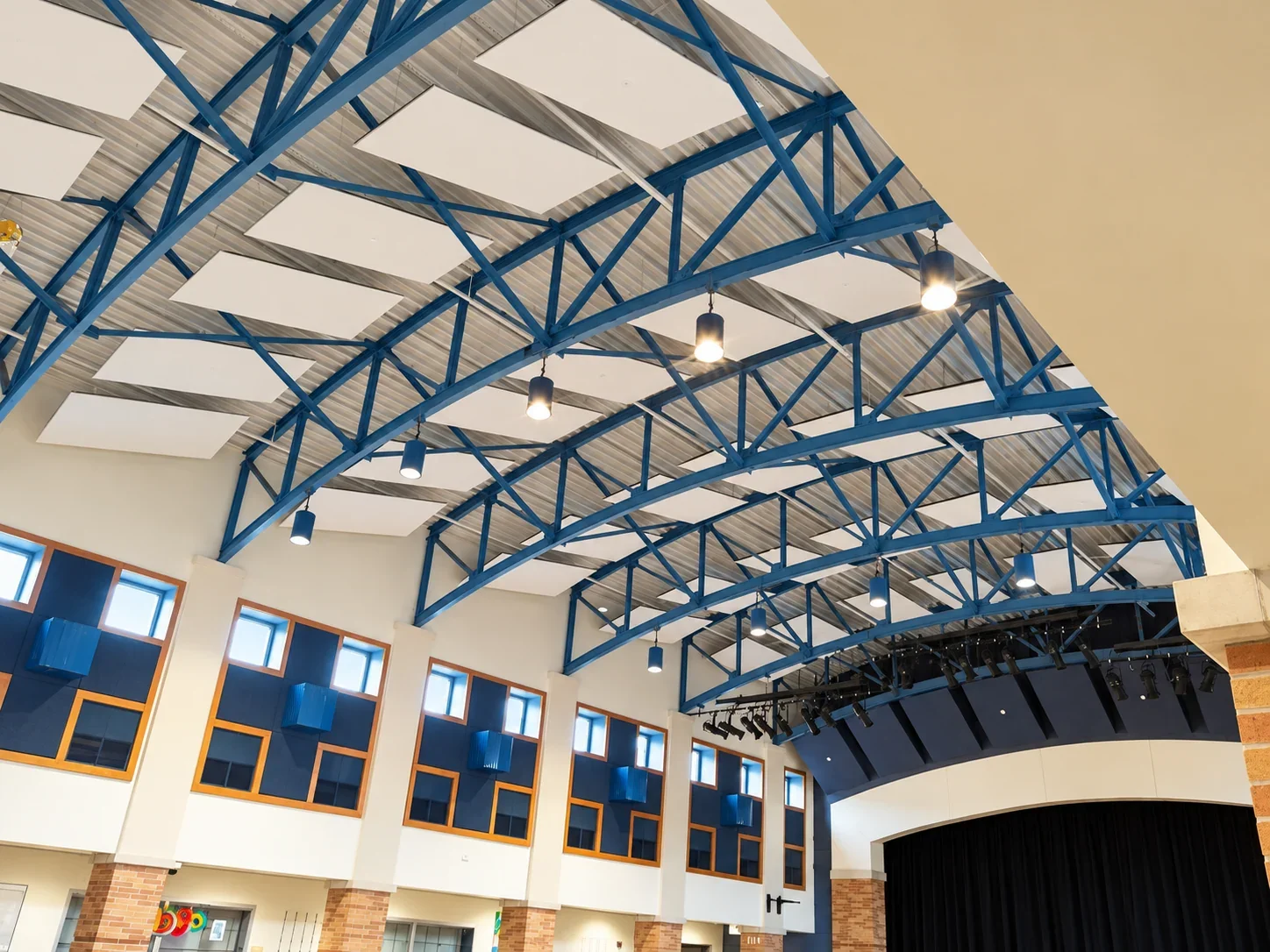LED pendant lights hanging from curved blue trusses above the stage opening in a Wilmington City Schools cafetorium