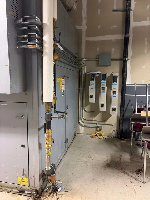 Three new variable frequency drives on the wall beside a heat recovery unit and its insulated piping at Cooper High School