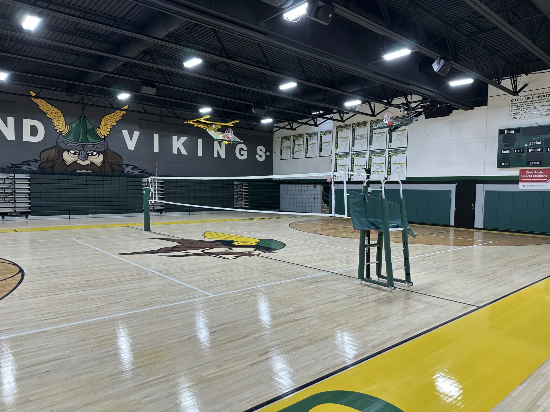 Renovated Northland High School gym with refinished maple floor, volleyball court set up and Vikings wall mural under new LED lights