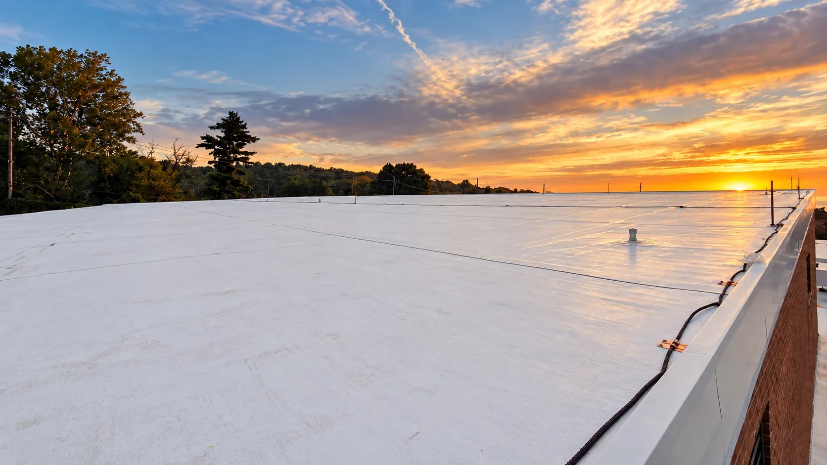 Sunset over the finished white TPO roof at Hamilton High School, with lightning protection running along the roof edge