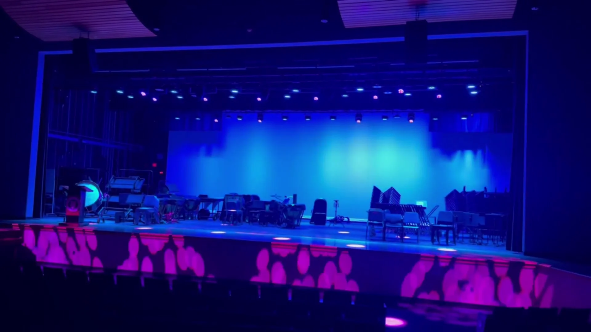 Video from the house of the Monroe High School stage under blue cyclorama light, with magenta gobo patterns across the apron